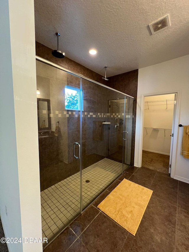 bathroom with tile patterned flooring, a shower with door, and a textured ceiling