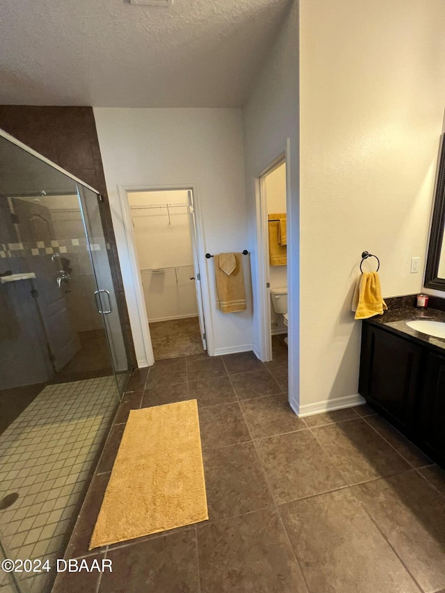 bathroom featuring tile patterned floors, a textured ceiling, an enclosed shower, toilet, and vanity