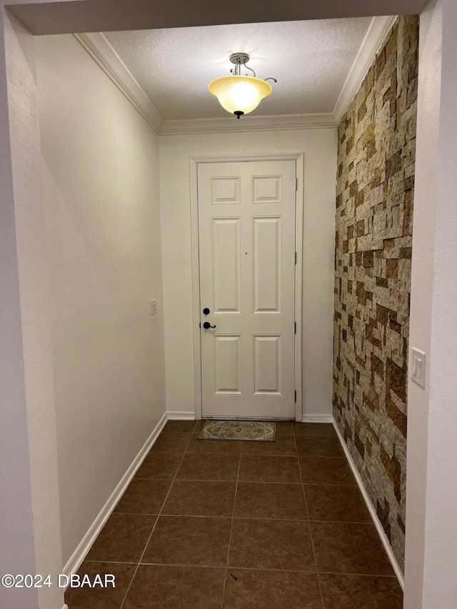 doorway to outside with a textured ceiling, dark tile patterned flooring, and ornamental molding