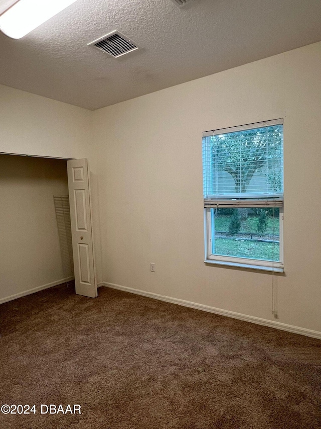 unfurnished bedroom with dark carpet and a textured ceiling