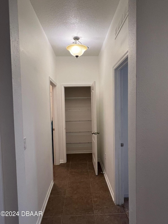 corridor featuring dark tile patterned floors and a textured ceiling