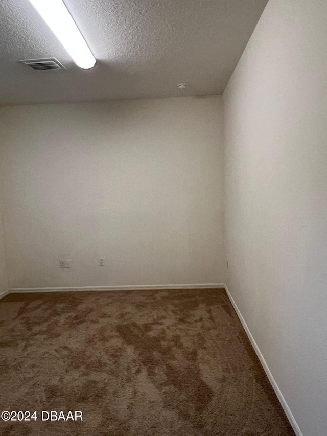 unfurnished room featuring a textured ceiling and dark carpet