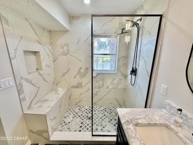full bath featuring a textured ceiling, tiled shower, and vanity