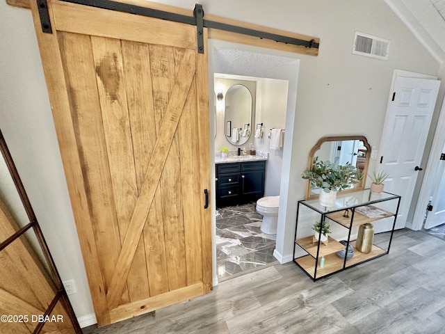 hallway featuring a barn door, a sink, baseboards, wood finished floors, and visible vents