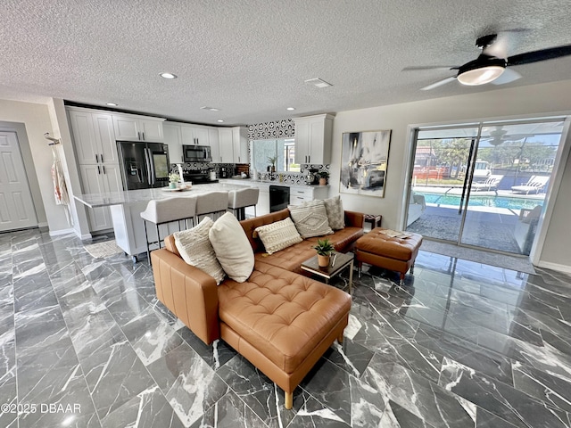 living room with ceiling fan, a textured ceiling, baseboards, marble finish floor, and recessed lighting