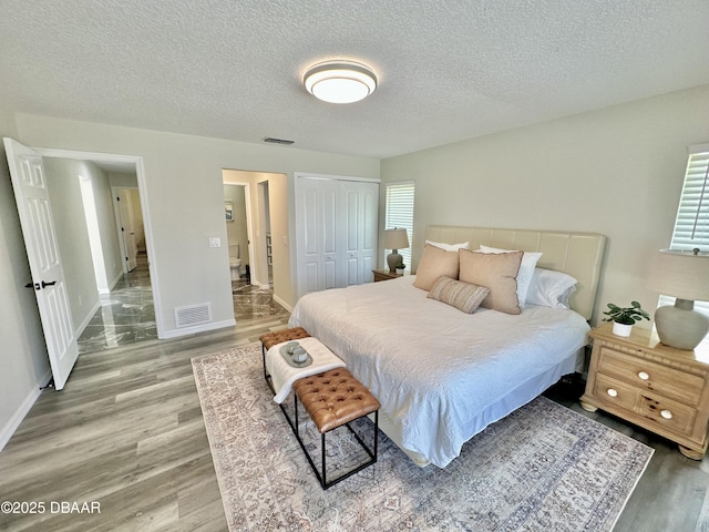 bedroom featuring a textured ceiling, baseboards, light wood-type flooring, visible vents, and a closet