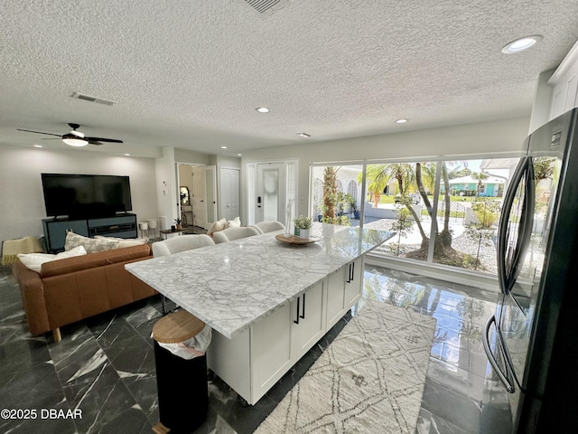 kitchen featuring visible vents, freestanding refrigerator, marble finish floor, a textured ceiling, and white cabinets