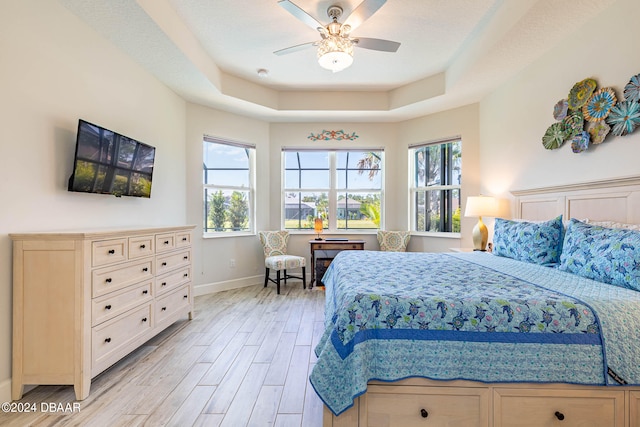 bedroom featuring ceiling fan, a raised ceiling, and light hardwood / wood-style flooring