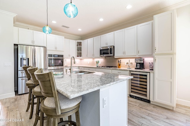 kitchen with white cabinetry, appliances with stainless steel finishes, an island with sink, beverage cooler, and pendant lighting