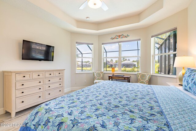 bedroom with light hardwood / wood-style floors, ceiling fan, multiple windows, and a tray ceiling