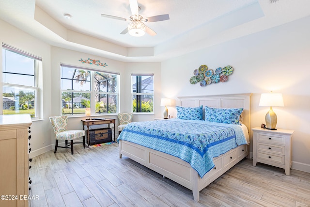 bedroom with ceiling fan, a tray ceiling, and light hardwood / wood-style floors