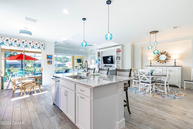 kitchen featuring light stone counters, white cabinetry, sink, an island with sink, and light hardwood / wood-style flooring