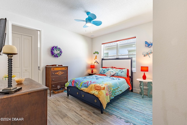 bedroom featuring a closet, light hardwood / wood-style floors, a textured ceiling, and ceiling fan