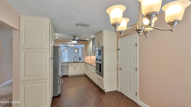 kitchen with kitchen peninsula, appliances with stainless steel finishes, ceiling fan with notable chandelier, sink, and dark hardwood / wood-style floors