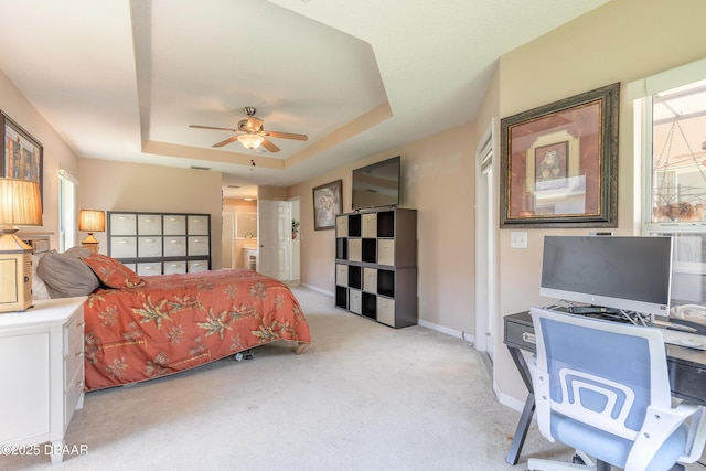 bedroom featuring baseboards, light carpet, connected bathroom, a tray ceiling, and ceiling fan