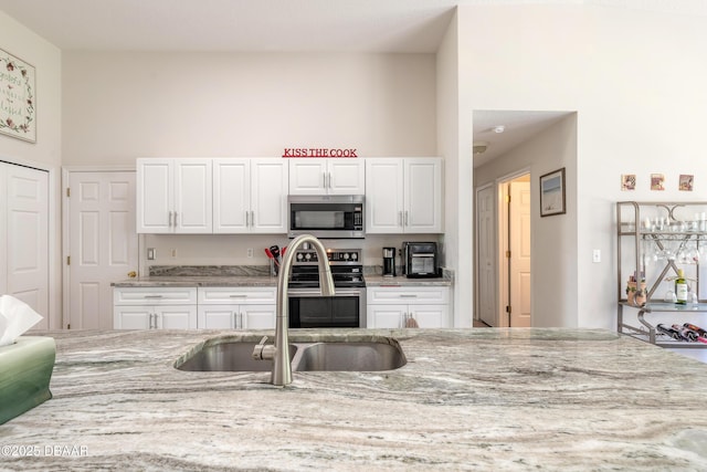 kitchen featuring white cabinets, appliances with stainless steel finishes, a sink, and light stone countertops