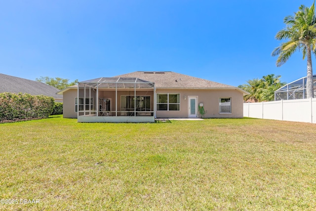 back of property with a yard, stucco siding, fence, and glass enclosure