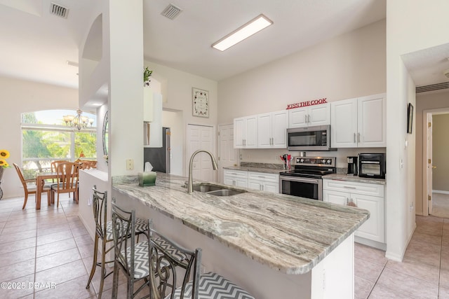 kitchen with a towering ceiling, a breakfast bar, a peninsula, visible vents, and appliances with stainless steel finishes