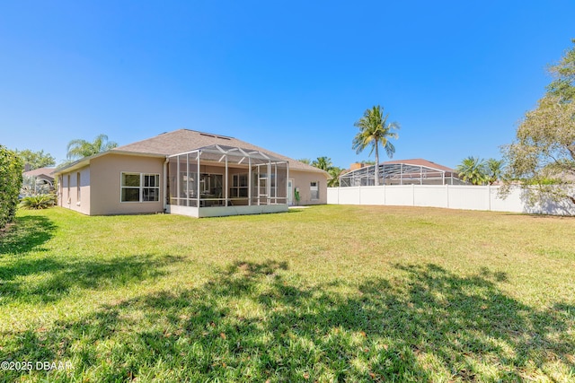 rear view of house with a lanai, a yard, and fence