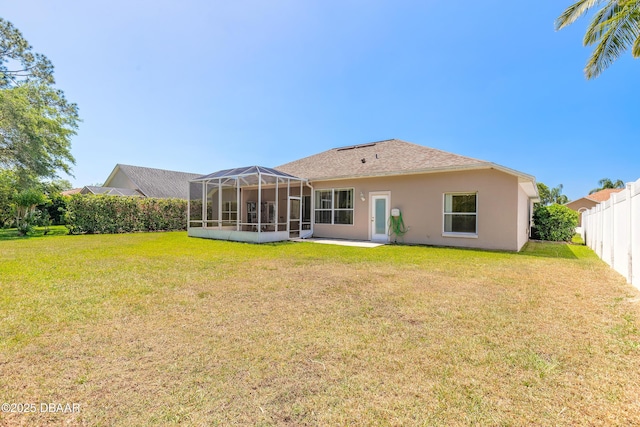 rear view of property with a yard, stucco siding, glass enclosure, and fence