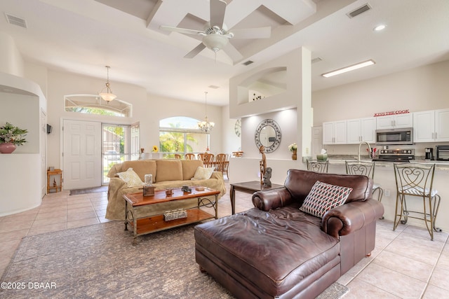 living room with light tile patterned floors, visible vents, ceiling fan with notable chandelier, and a towering ceiling