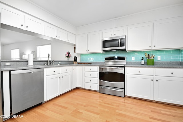 kitchen featuring sink, stainless steel appliances, white cabinets, decorative backsplash, and light wood-type flooring