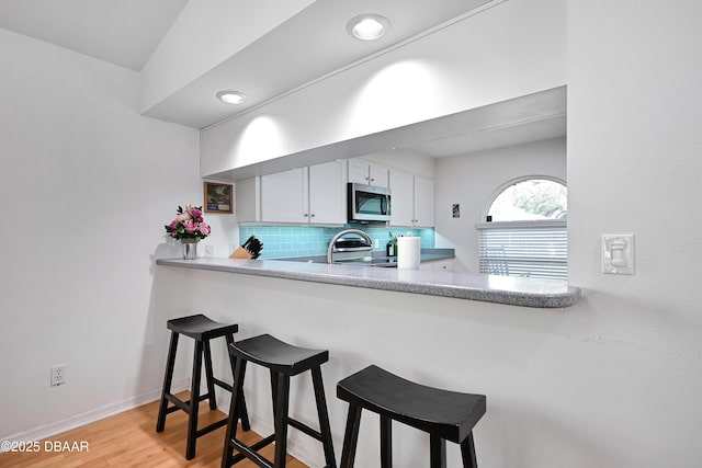 kitchen featuring backsplash, a kitchen breakfast bar, stainless steel appliances, light hardwood / wood-style floors, and white cabinets