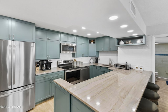 kitchen featuring light stone counters, sink, appliances with stainless steel finishes, and light hardwood / wood-style flooring