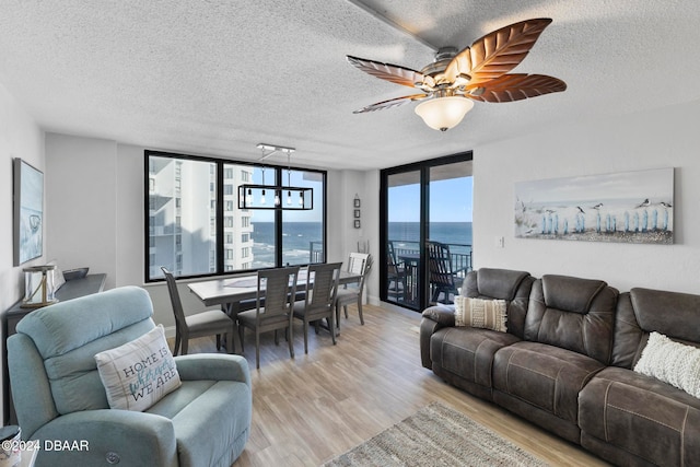 living room featuring a textured ceiling, a water view, light hardwood / wood-style flooring, and ceiling fan