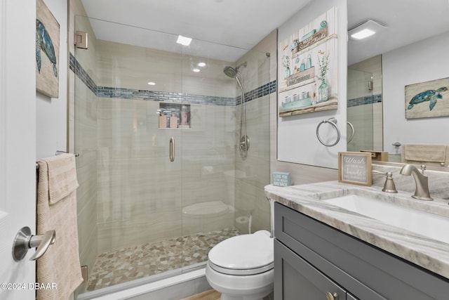 bathroom featuring a shower with door, vanity, and toilet