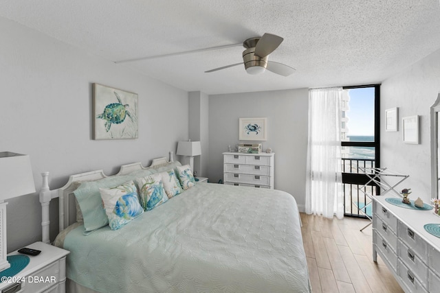 bedroom with ceiling fan, expansive windows, light hardwood / wood-style floors, and a textured ceiling