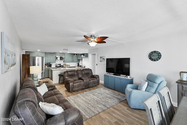 living room featuring ceiling fan, sink, light wood-type flooring, and a textured ceiling