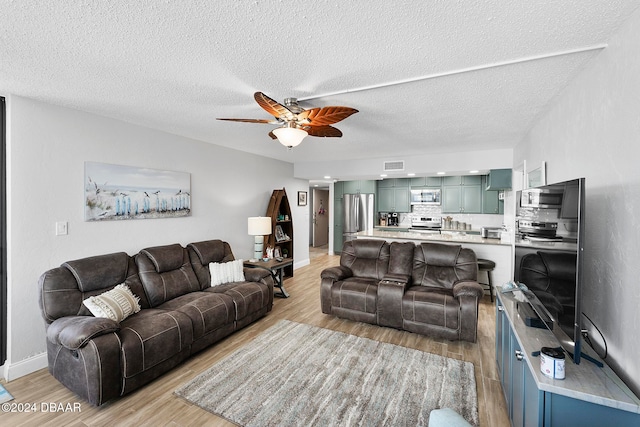 living room featuring ceiling fan, light hardwood / wood-style floors, and a textured ceiling