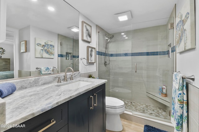 bathroom featuring wood-type flooring, vanity, toilet, and a shower with shower door