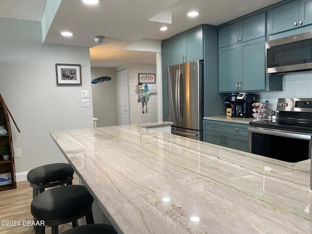 kitchen featuring tasteful backsplash, light stone counters, a textured ceiling, a breakfast bar, and appliances with stainless steel finishes