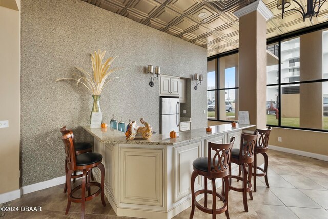 kitchen featuring a breakfast bar area, a wealth of natural light, refrigerator, and light stone countertops