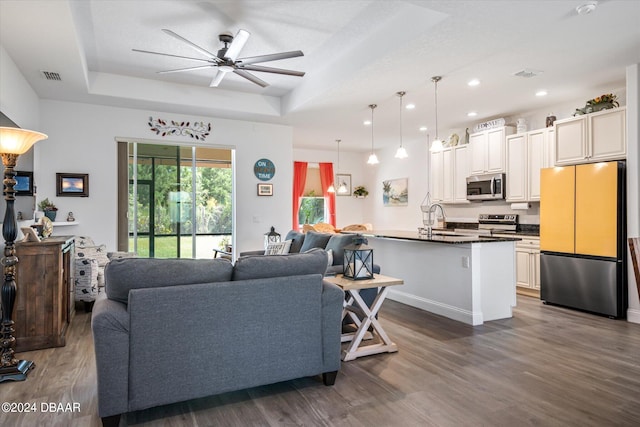 living room featuring dark wood-type flooring, ceiling fan, and a tray ceiling