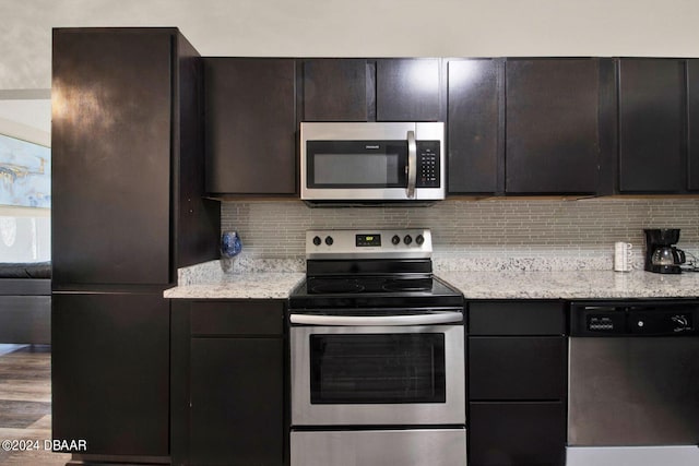 kitchen featuring wood-type flooring, dark brown cabinetry, stainless steel appliances, and light stone counters