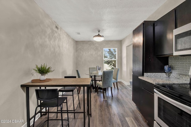 kitchen featuring light stone countertops, backsplash, a textured ceiling, stainless steel appliances, and dark hardwood / wood-style floors