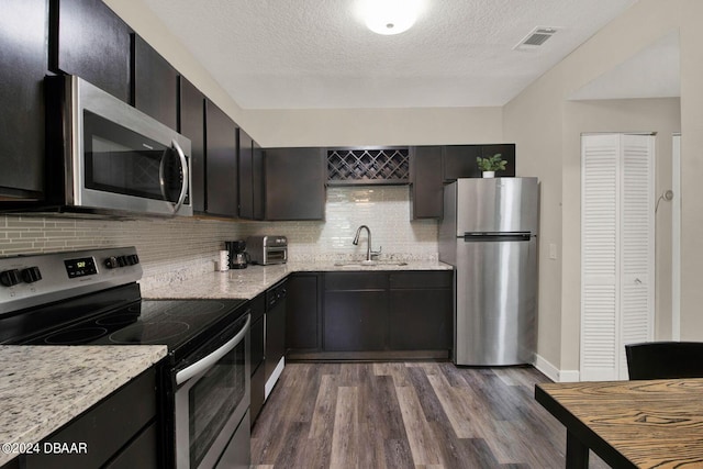 kitchen featuring hardwood / wood-style flooring, a textured ceiling, tasteful backsplash, light stone counters, and stainless steel appliances