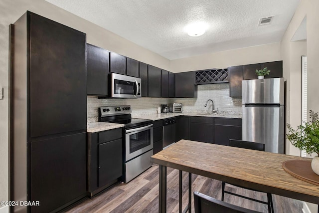 kitchen featuring appliances with stainless steel finishes, backsplash, light stone counters, a textured ceiling, and light hardwood / wood-style flooring