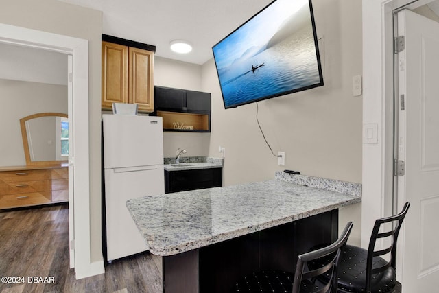 kitchen with kitchen peninsula, a kitchen breakfast bar, white fridge, and dark hardwood / wood-style floors