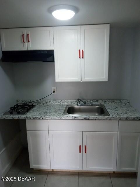 kitchen featuring sink, white cabinets, light tile patterned floors, light stone counters, and black gas stovetop