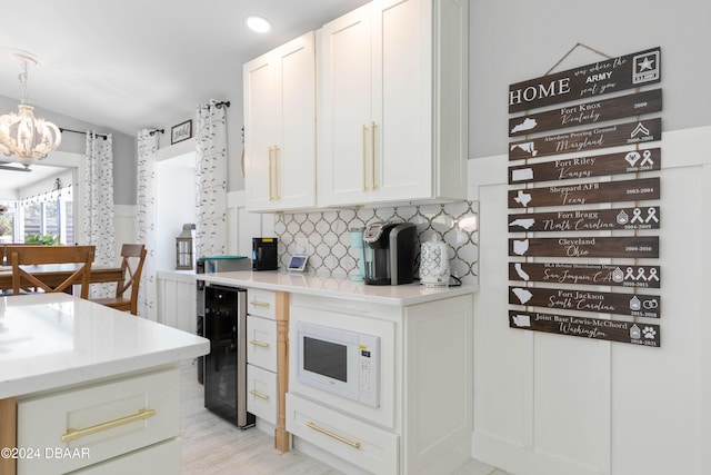 kitchen with white microwave, white cabinetry, a chandelier, wine cooler, and hanging light fixtures