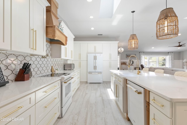 kitchen featuring white appliances, decorative light fixtures, light hardwood / wood-style flooring, and a center island with sink