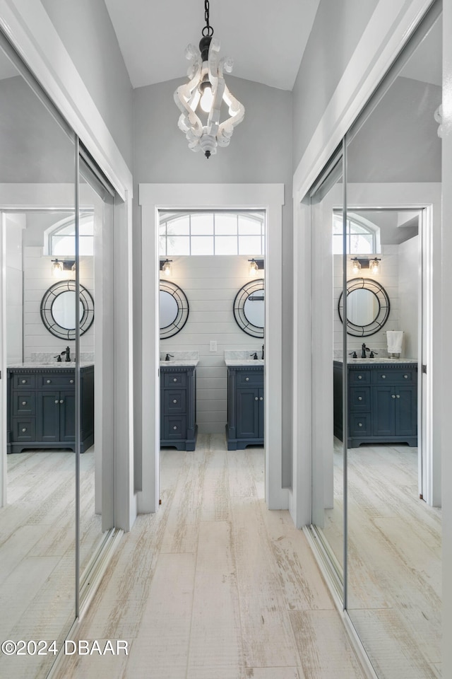 corridor featuring sink, a notable chandelier, light hardwood / wood-style floors, lofted ceiling, and tile walls