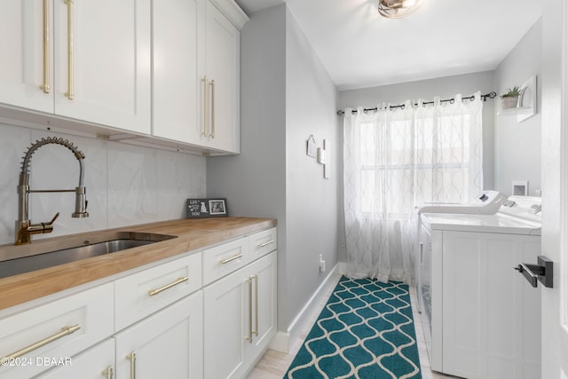 clothes washing area with washer and clothes dryer, cabinets, and sink