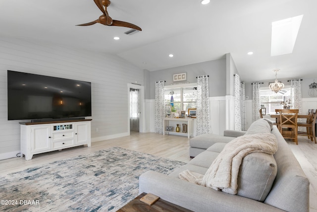 living room featuring vaulted ceiling with skylight, ceiling fan, and light wood-type flooring