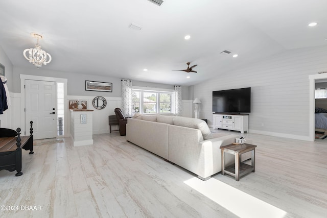 living room with ceiling fan with notable chandelier, light hardwood / wood-style flooring, and vaulted ceiling