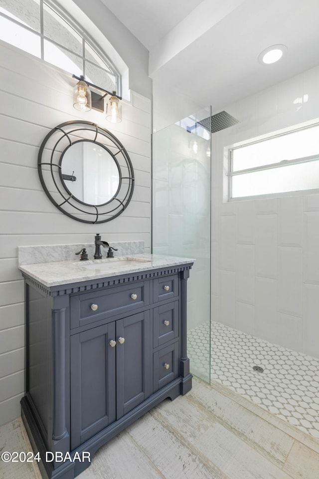 bathroom featuring tiled shower, vanity, and wood walls